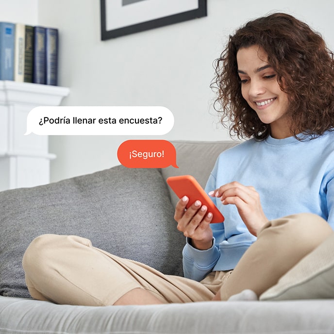 Una niña sentada en un sofá, respondiendo una encuesta en su celular