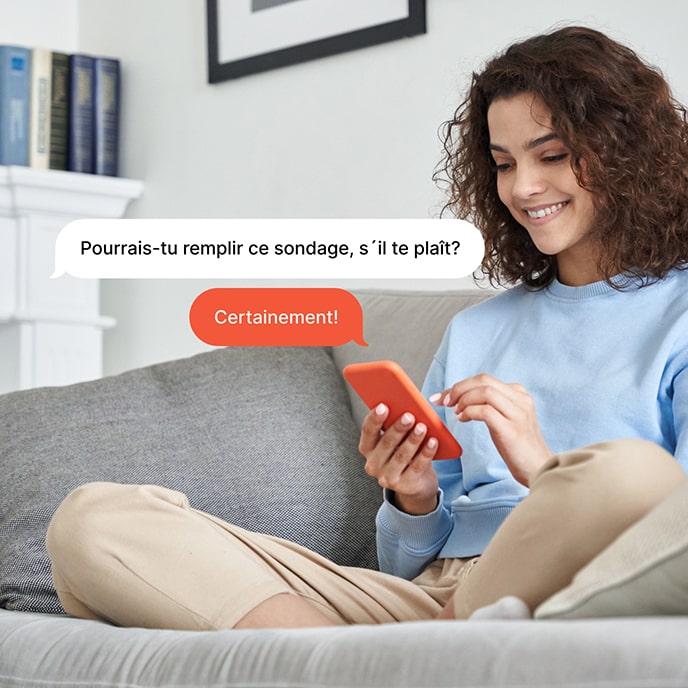 A woman sitting on a couch, answering a survey on her cellphone