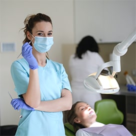 Zdjęcie dentysty patrzącego w kamerę z pacjentem w tle